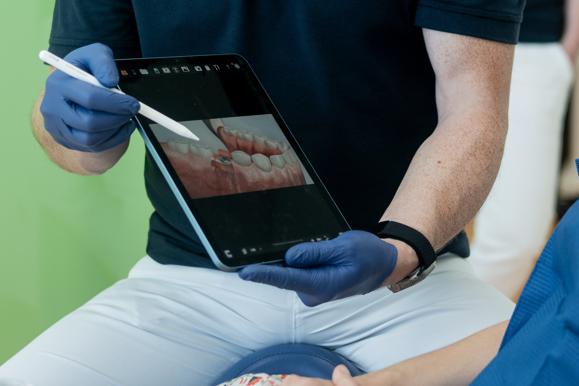 Zahnarzt zeigt mit einem Stift auf ein digitales 3D-Modell eines Gebisses auf einem Tablet