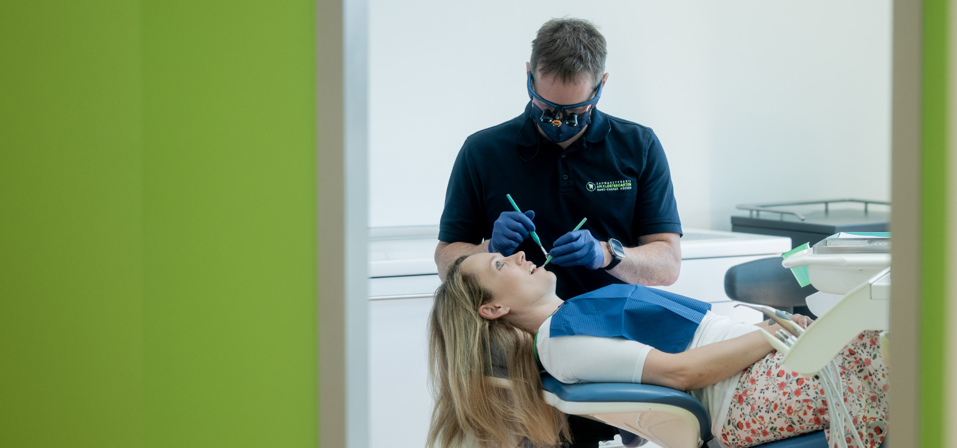 Zahnarzt behandelt eine Patientin im Behandlungszimmer, gesehen durch die offene Tür